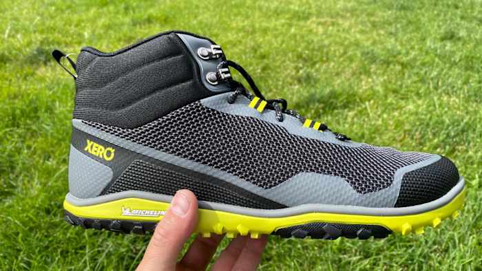 xero-shoes-scrambler-mid-grey-lime-green-hand-holding-side-view-grass-background